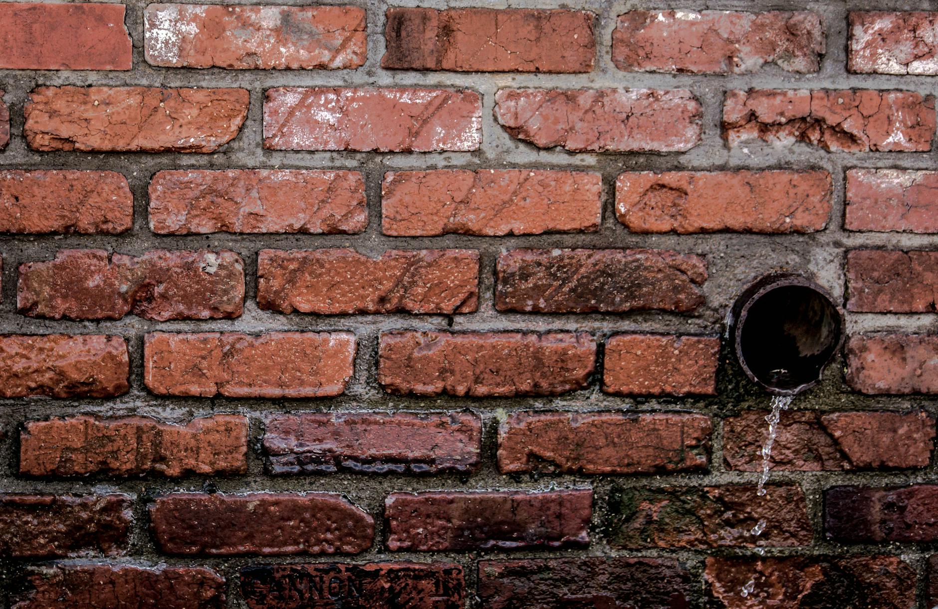 Close-up of a red brick wall with water flowing from a drain, showcasing texture and patterns.