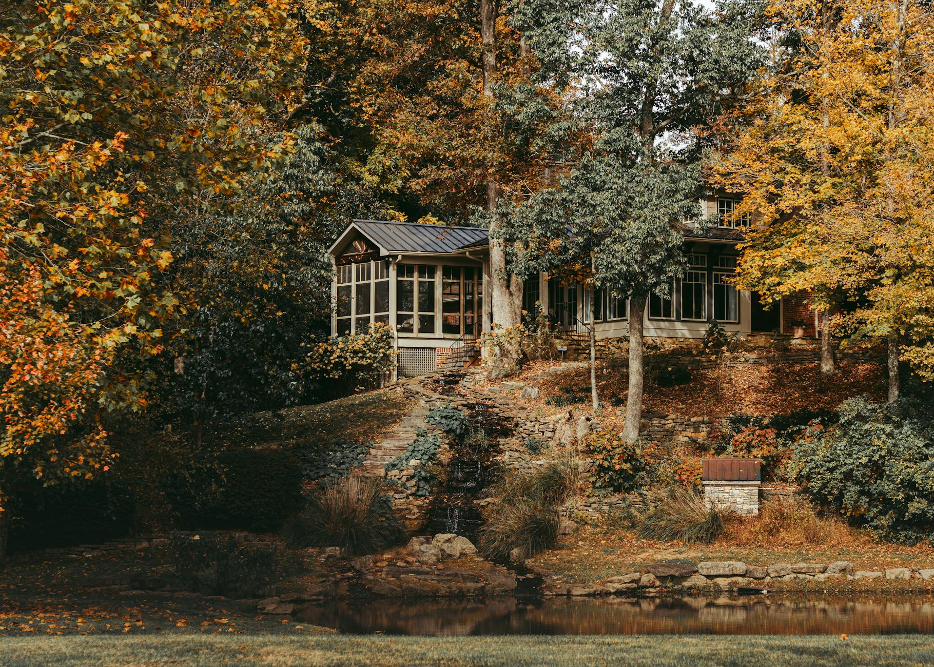 Beautiful fall scene of a cozy cottage surrounded by colorful autumn trees by a tranquil lake.