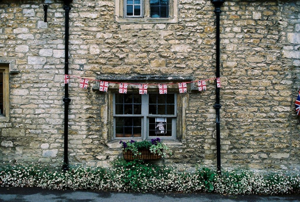 Rustic stone facade of a traditional British house with flag bunting and flowers.