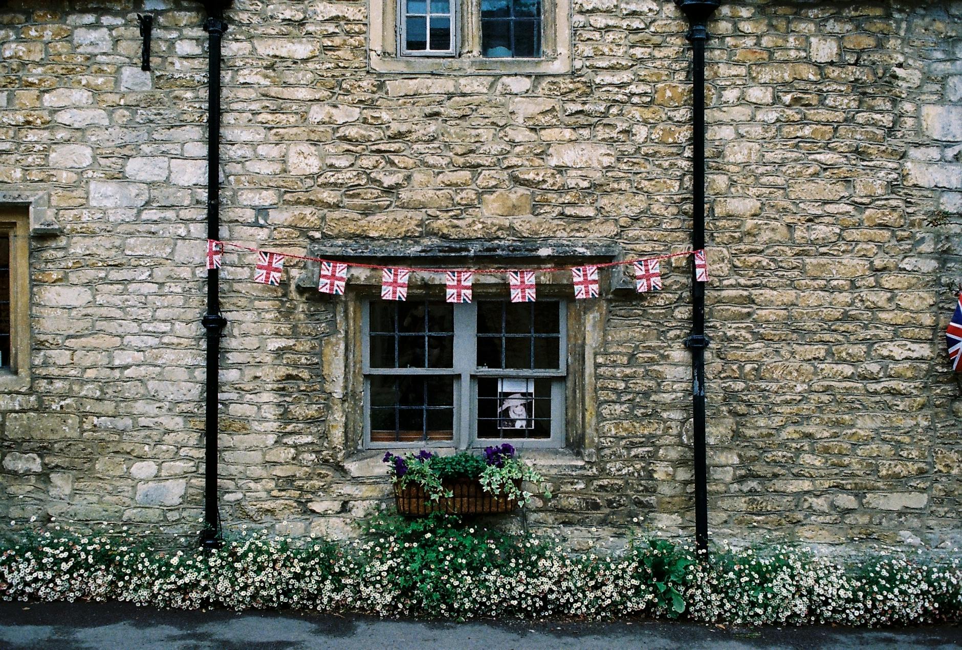 Rustic stone facade of a traditional British house with flag bunting and flowers.