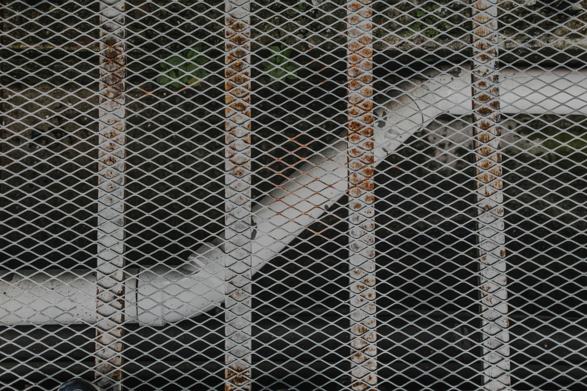Close-up view of a rusty metal grid with a pipe in the background, showcasing industrial textures.