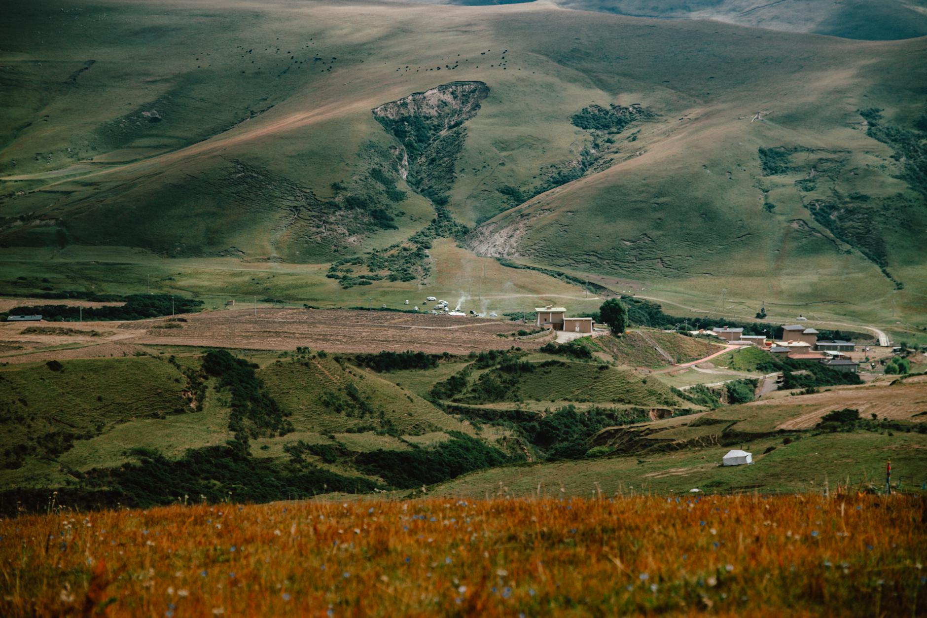 Picturesque rural landscape showcasing rolling hills and small settlement during daytime.