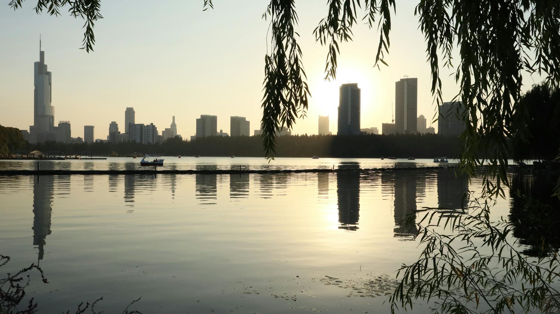 Cityscape with sunset reflections over water and silhouettes of skyscrapers.