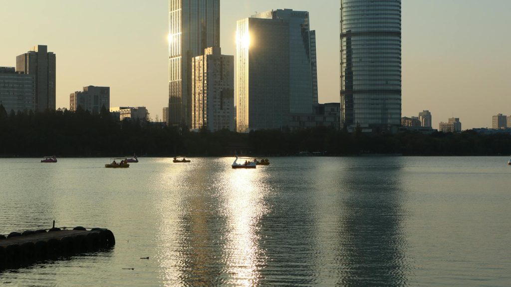 Skyscrapers reflecting on tranquil water during sunrise with pedal boats.