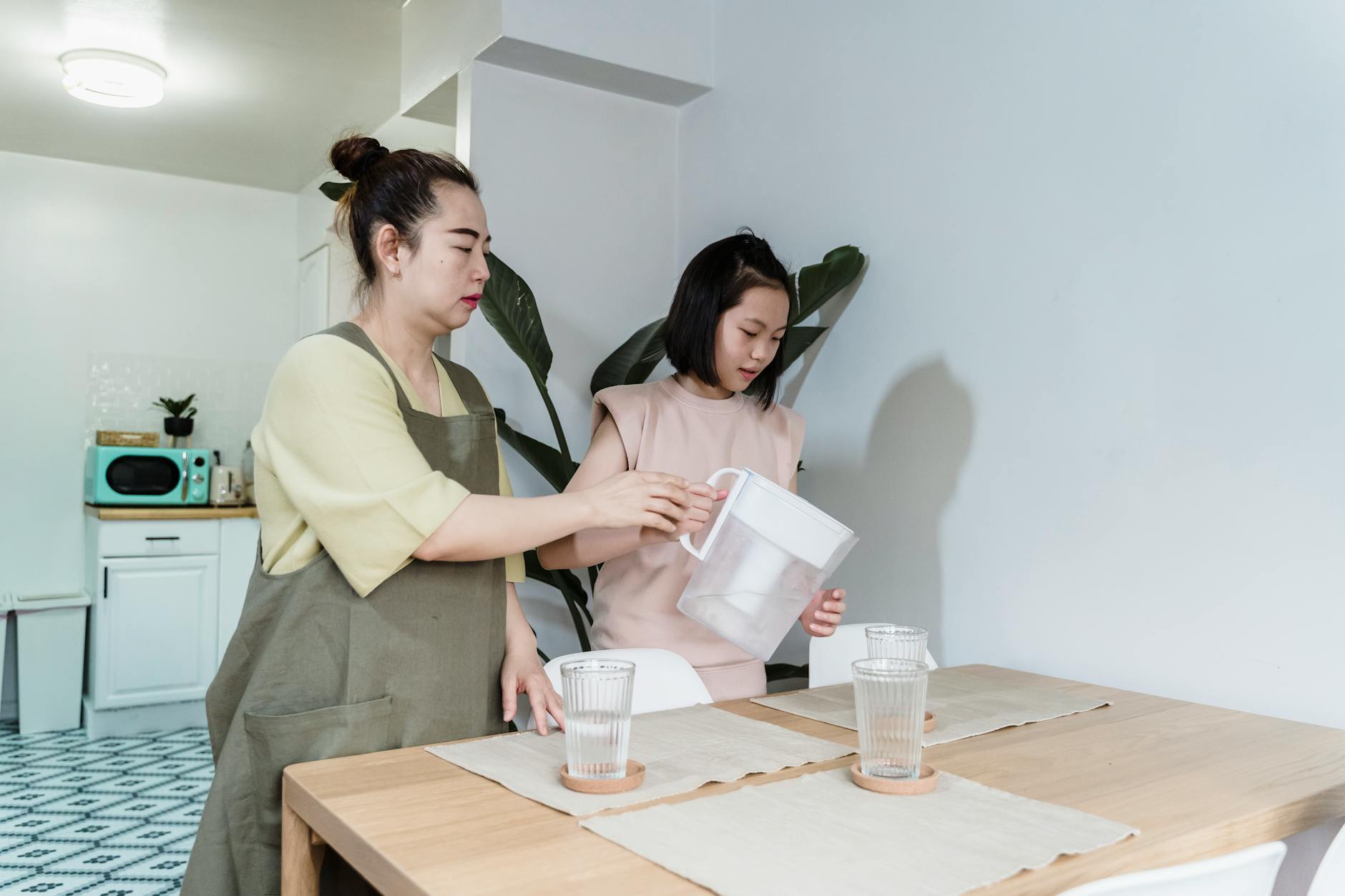 A mother and daughter engaging in bonding activity by preparing water at the kitchen table.