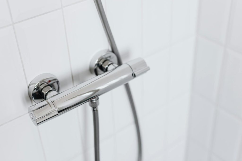 Modern chrome shower faucet on white tiled wall, elegant and clean design.