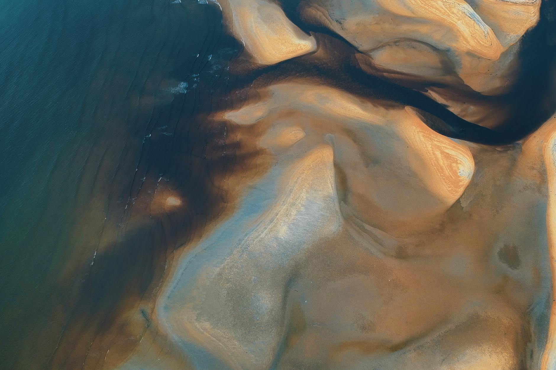 Aerial photograph capturing intricate sand and water patterns on a Malaysian coast.