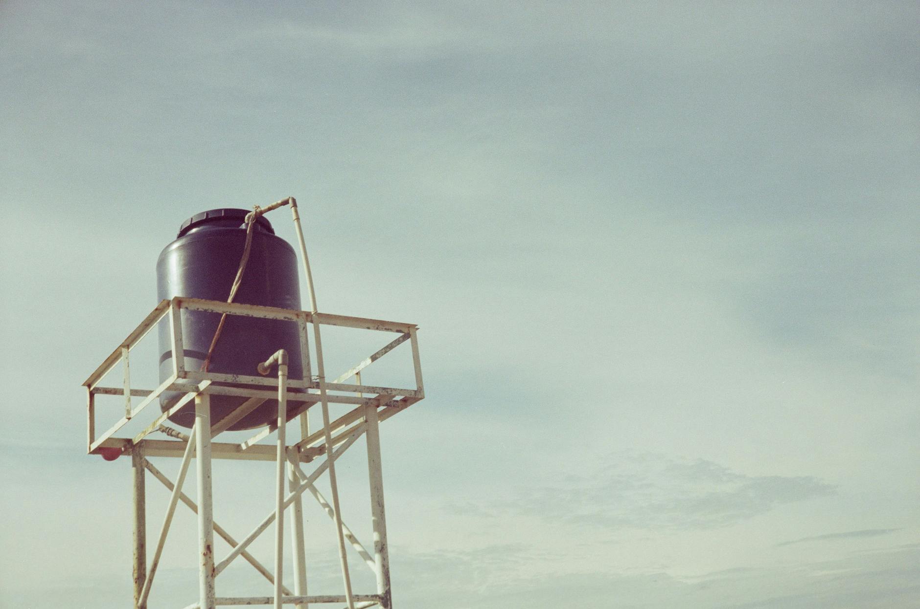 An industrial water tank atop a metal frame against a clear sky, showcasing infrastructure design.