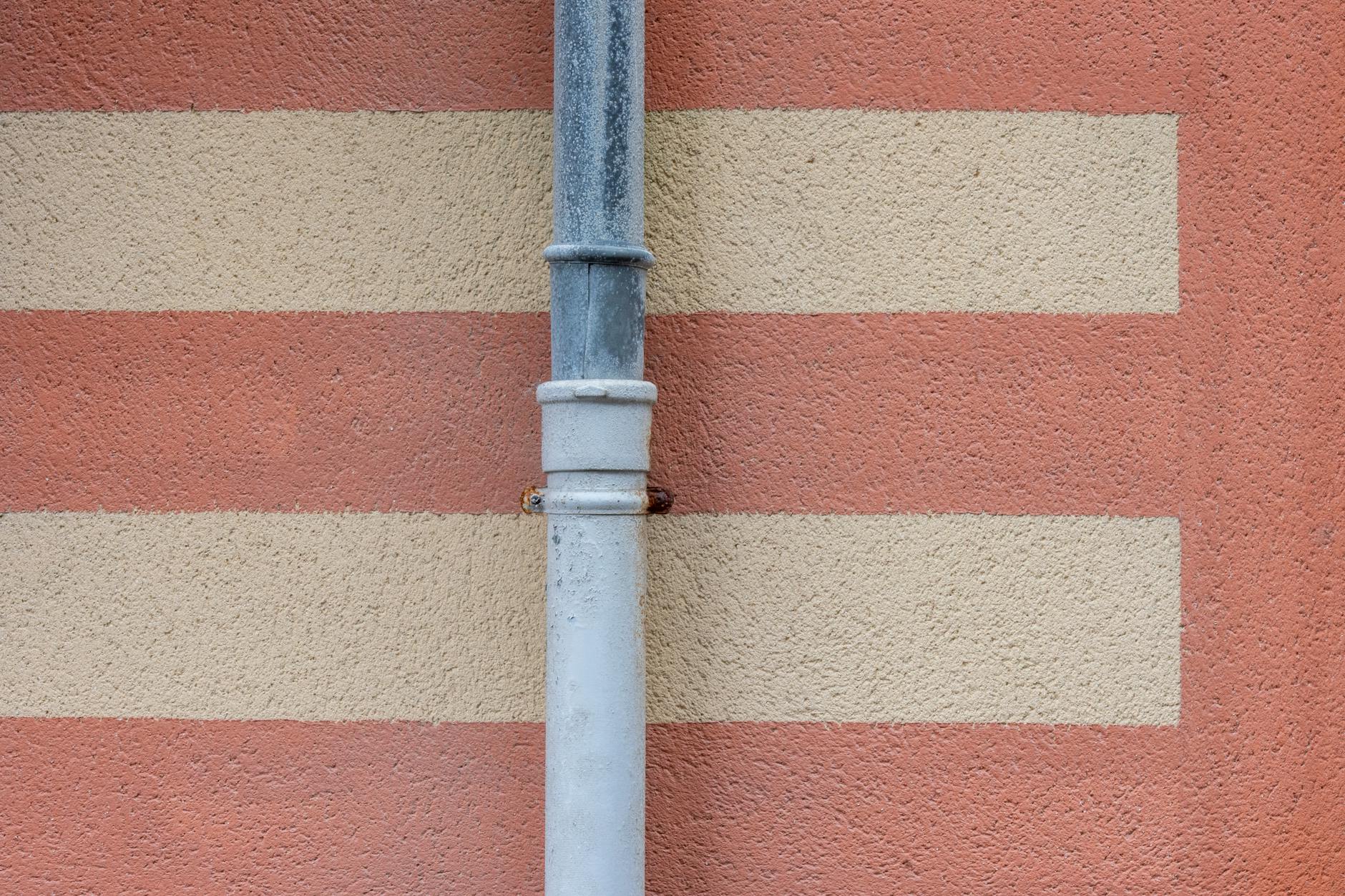 Close-up of a weathered metal drainpipe on a textured, striped wall.