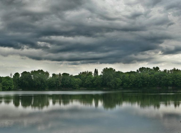 Stormy clouds over a peaceful lake reflect a moody and dramatic atmosphere.