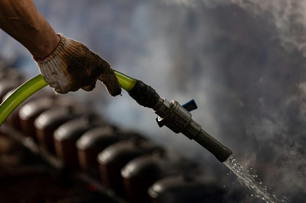 A gloved hand handling an industrial water hose with steam in the background.
