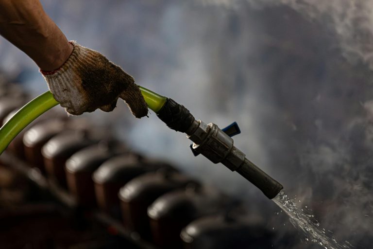 A gloved hand handling an industrial water hose with steam in the background.