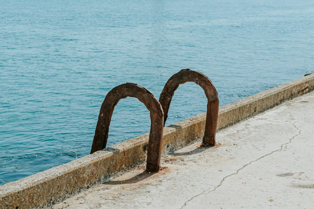 Weathered metal ladder on a concrete pier facing a calm blue sea.